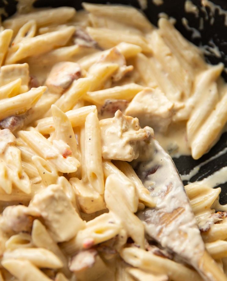 close up shot of wooden spoon digging into skillet of pasta