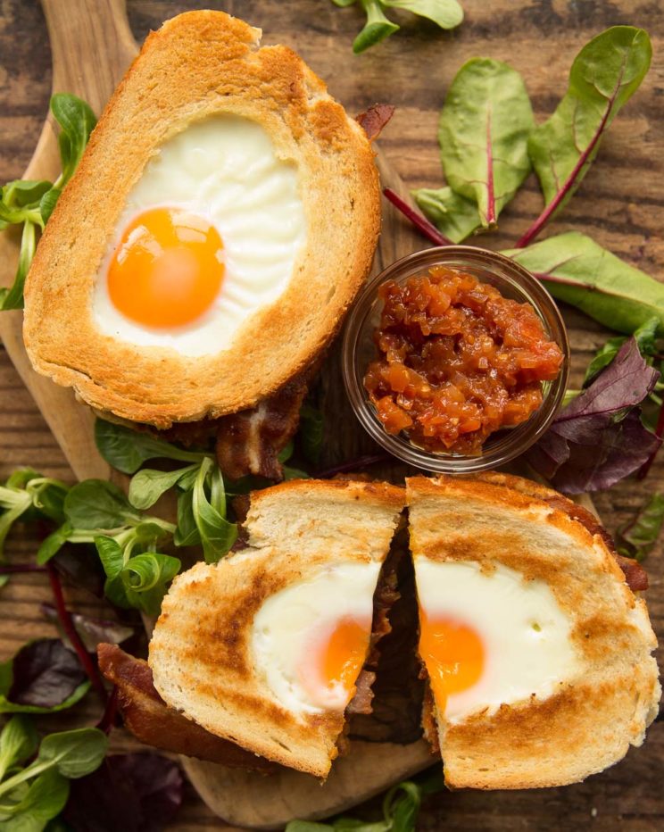 overhead shot of two egg in hole sandwiches with chutney and salad to garnish