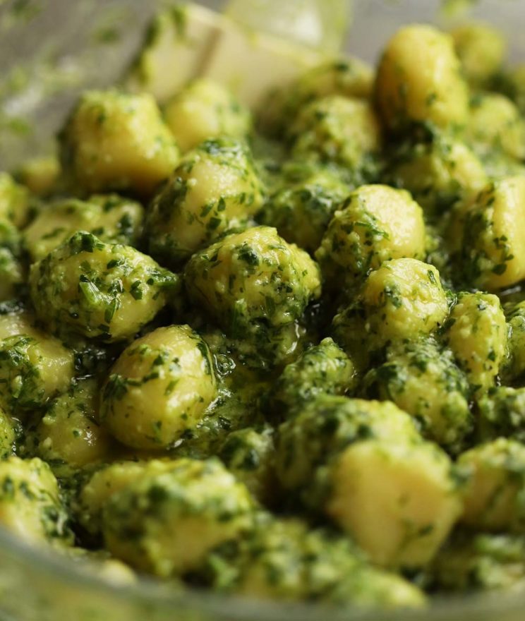 closeup shot of gnocchi coated in pesto in big glass bowl