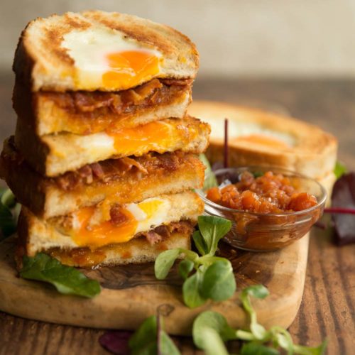 egg and bacon sandwiches stacked on top of each other on wooden board with salad to garnish