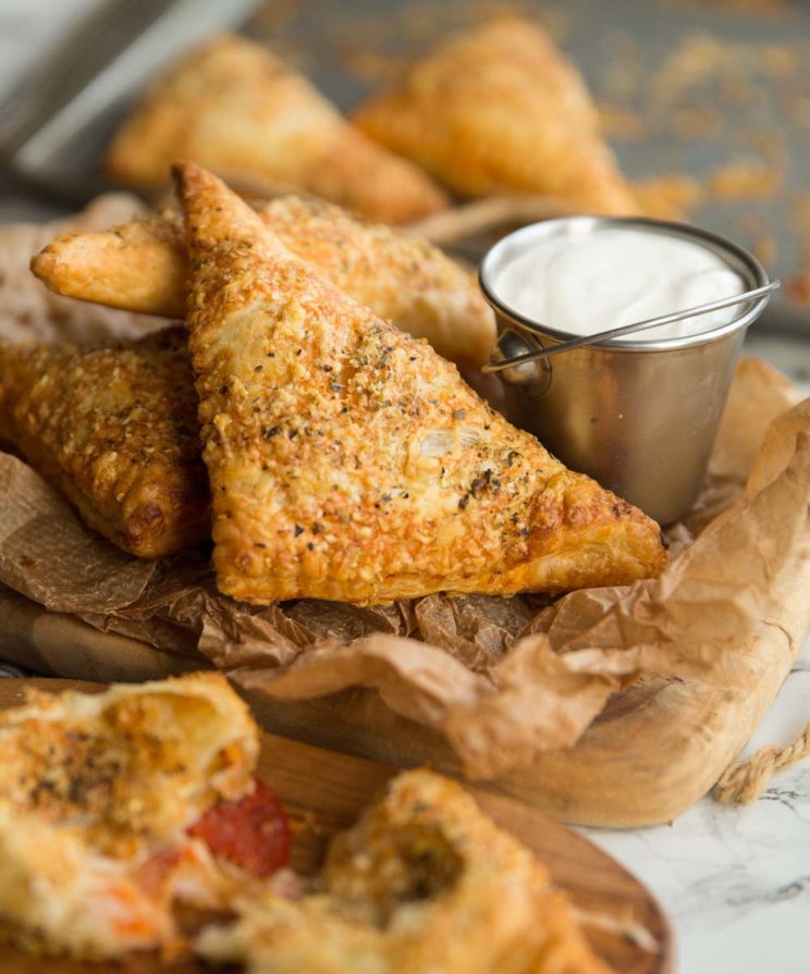 side shot of pizza pockets on brown chopping board with dip