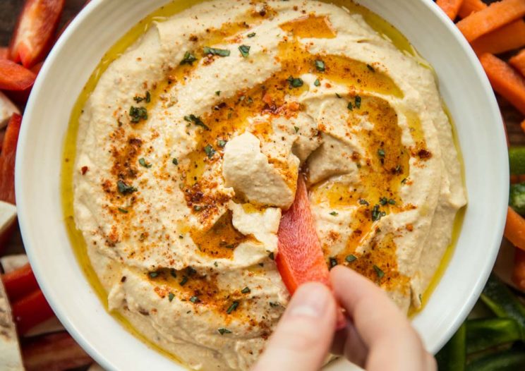 closeup shot of red pepper dipping into hummus