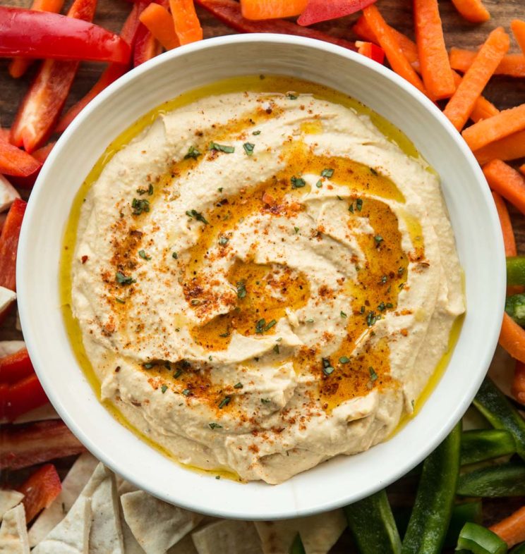 overhead shot of peri peri hummus surrounded by peppers, pita and carrot