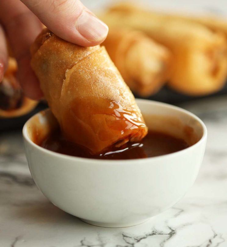 dunking chicken spring roll into pot of sweet and sour sauce
