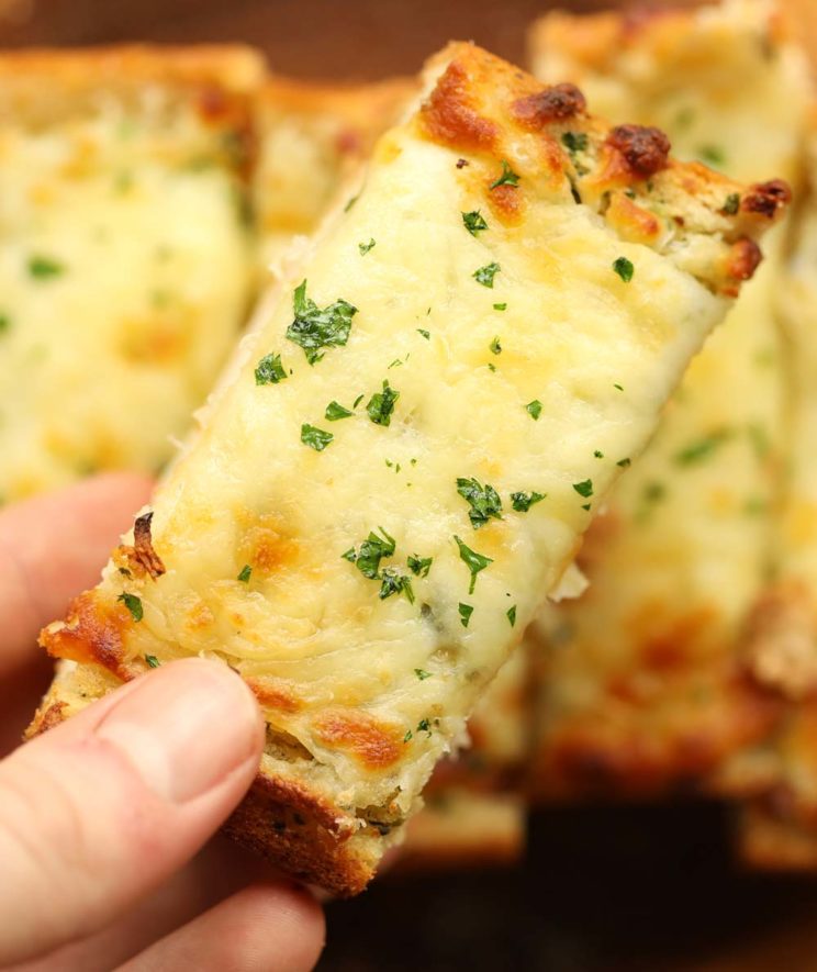 overhead closeup shot of cheesy garlic bread with load blurred in the background