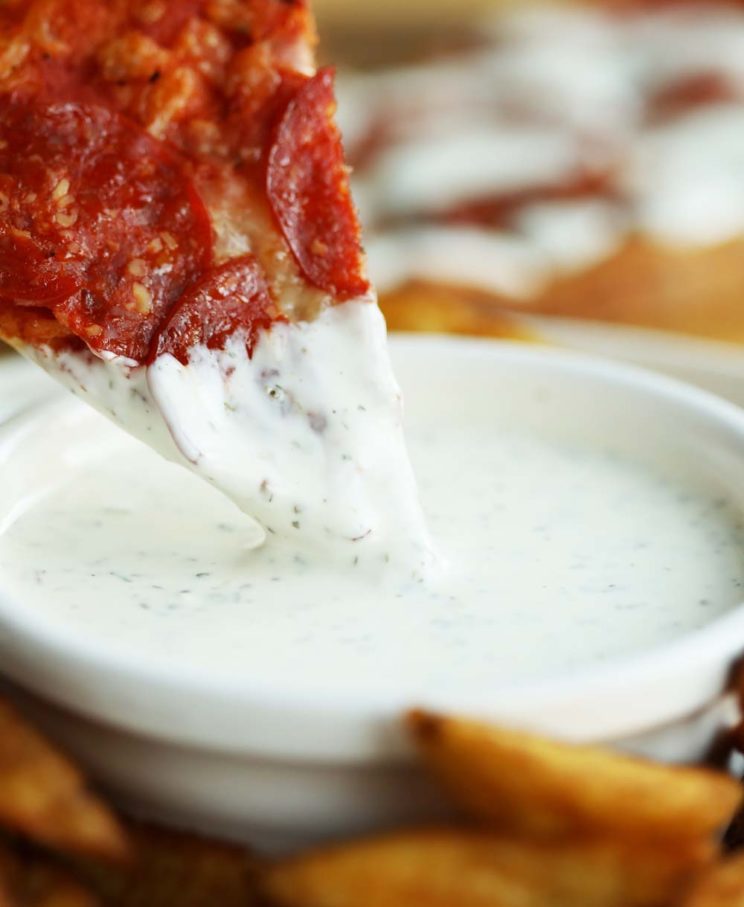 dunking pizza into pot of garlic and herb dip 