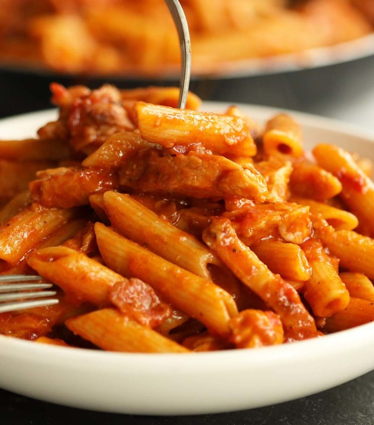 fork digging into pasta in white bowl with skillet blurred in background