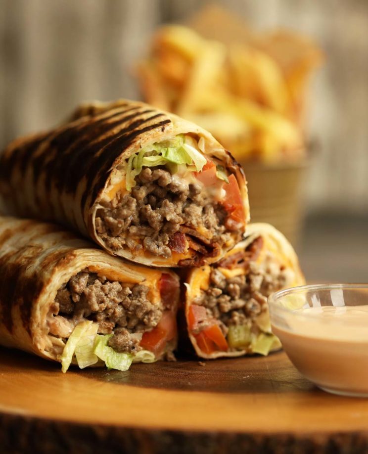 cheeseburger wraps stacked on top of each other on wooden board with fries blurred in background