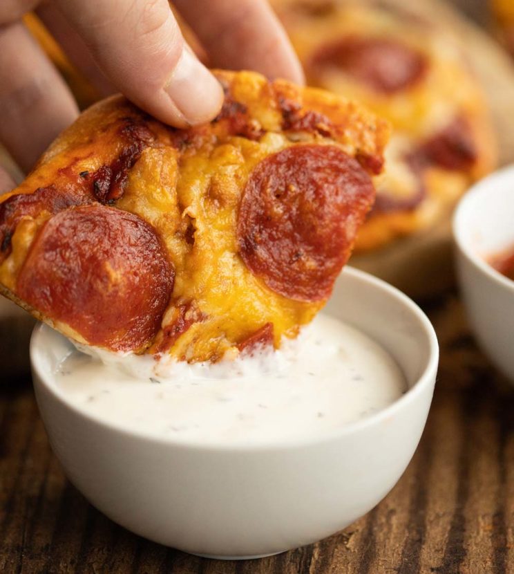 pepperoni pizza dunking into dip with full pizza blurred in the background