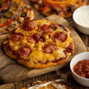 4 different pizzas, focus on one sat on wooden chopping board