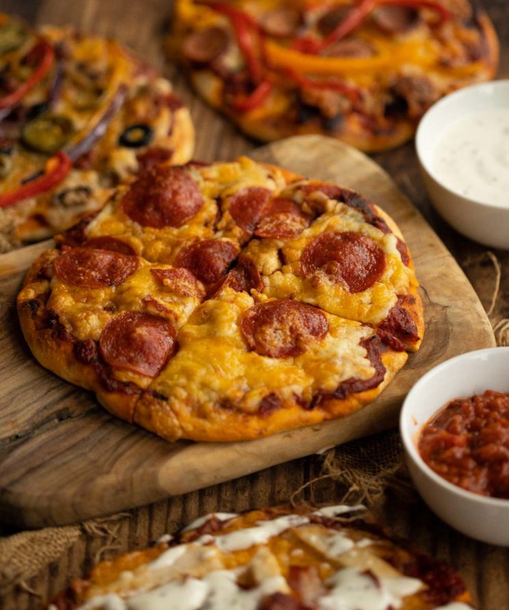 4 different pizzas, focus on one sat on wooden chopping board
