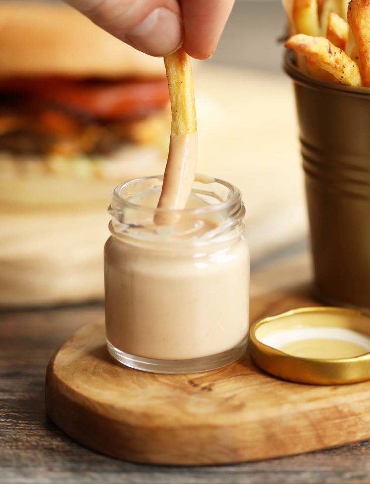 dunking french fries into small glass pot of burger sauce