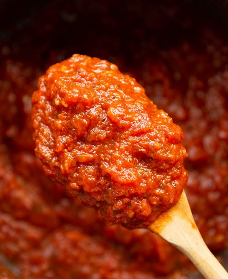 pizza sauce on wooden spoon with pot of pizza sauce blurred in background