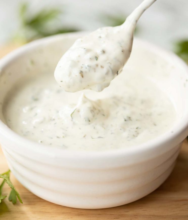 spoon dipping into small white pot of sauce