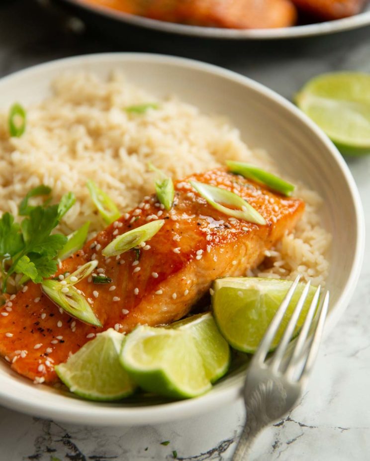 salmon in white bowl with rice garnished with sesame seeds, spring onion and lime wedges