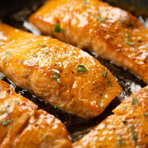 closeup of salmon in frying pan with glaze over it