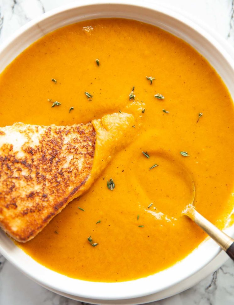 overhead shot of soup in a bowl with grilled cheese and spoon garnished with fresh thyme