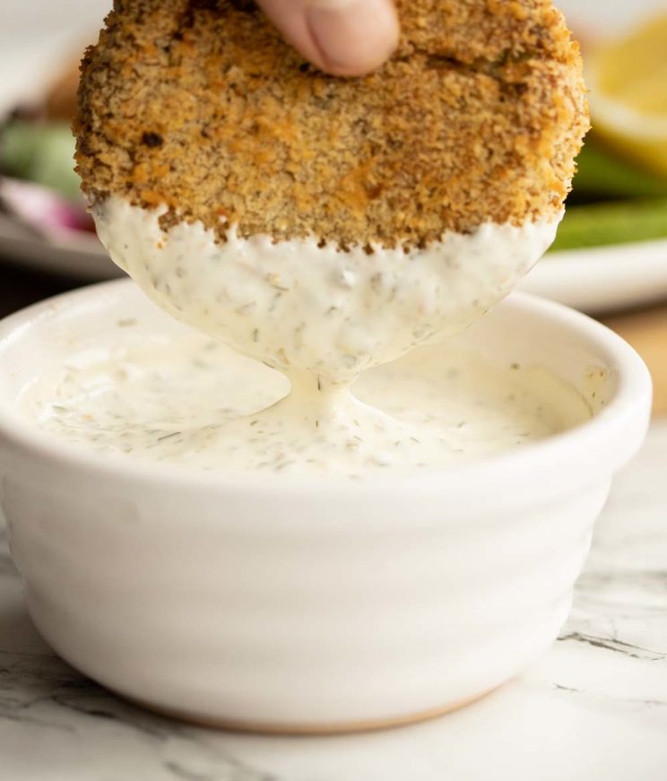 dunking tuna fish cakes into small white pot of tartare sauce