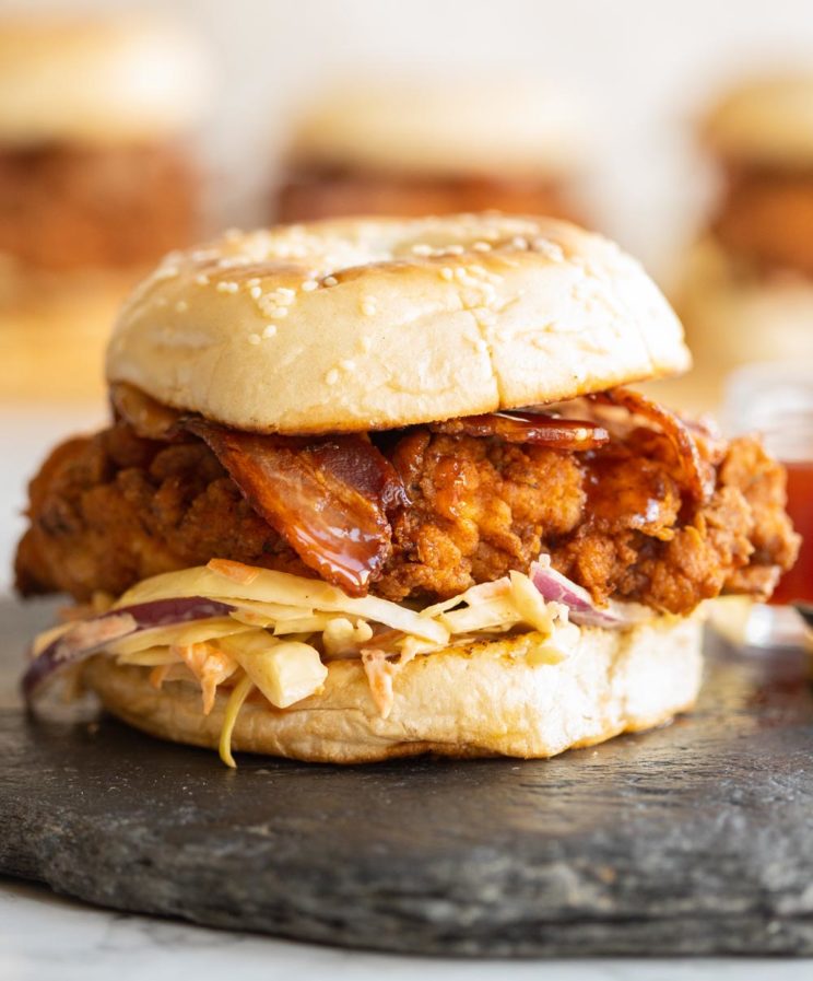 chicken burger sat on slate with 3 more blurred in the background