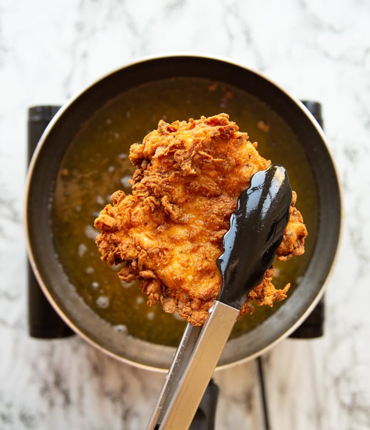 holding fried chicken above oil with tongs