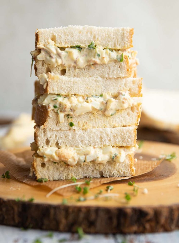 3 sandwiches stacked on each other on wooden board garnished with cress