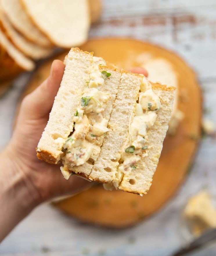 holding an open sandwich above wooden board with filling on show