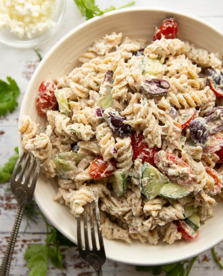 overhead shot of pasta salad in white bowl surround by fresh parsley