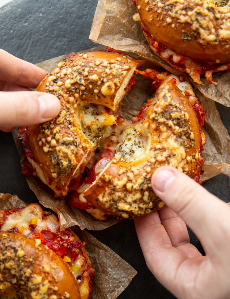 two hands pulling apart bagel with cheese pull in middle