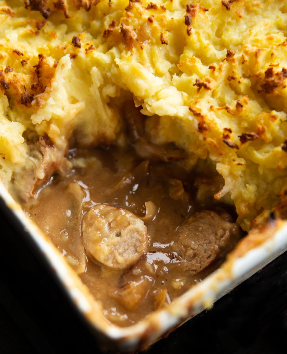 close up shot of sausage and gravy underneath mash fresh out the oven