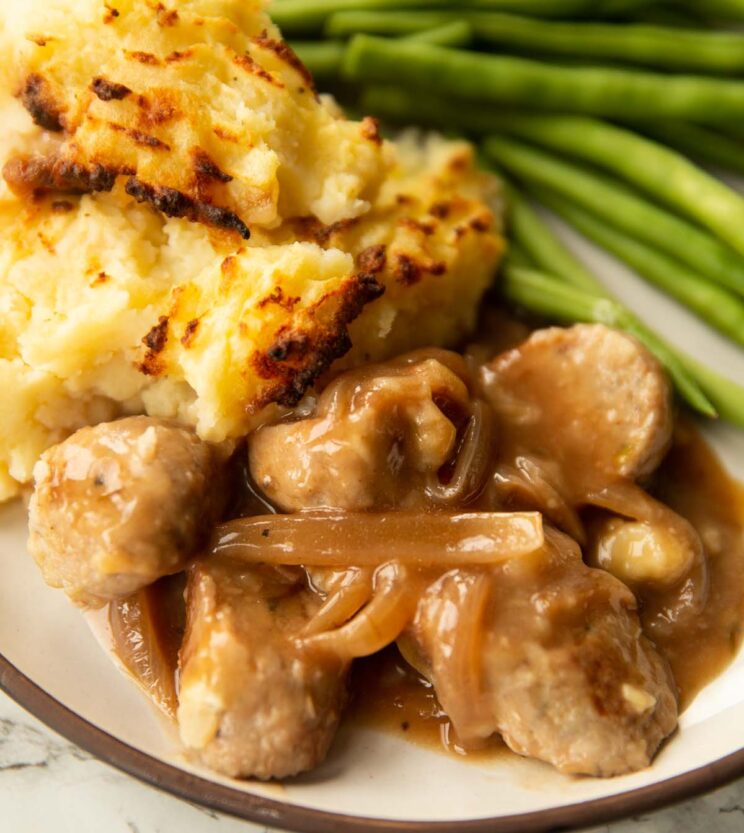 close up shot of sausage mash pie with green beans on small white plate