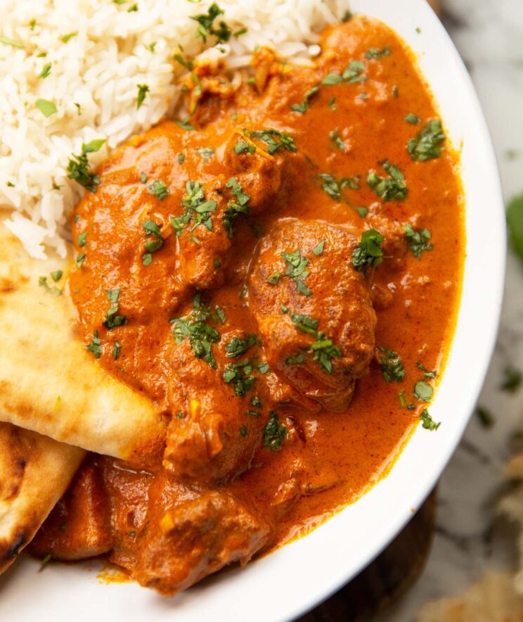 close up side shot of slow cooker curry in large white bowl with rice and naan bread 