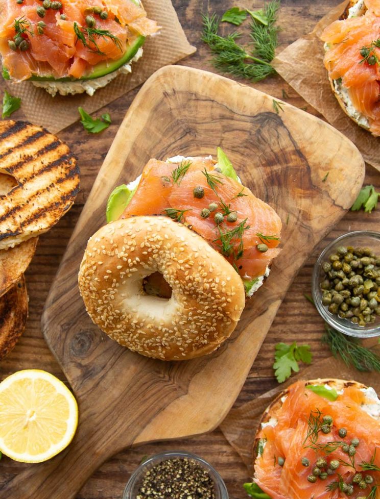 overhead shot of bagels on wooden board surrounded by ingredients and garnish
