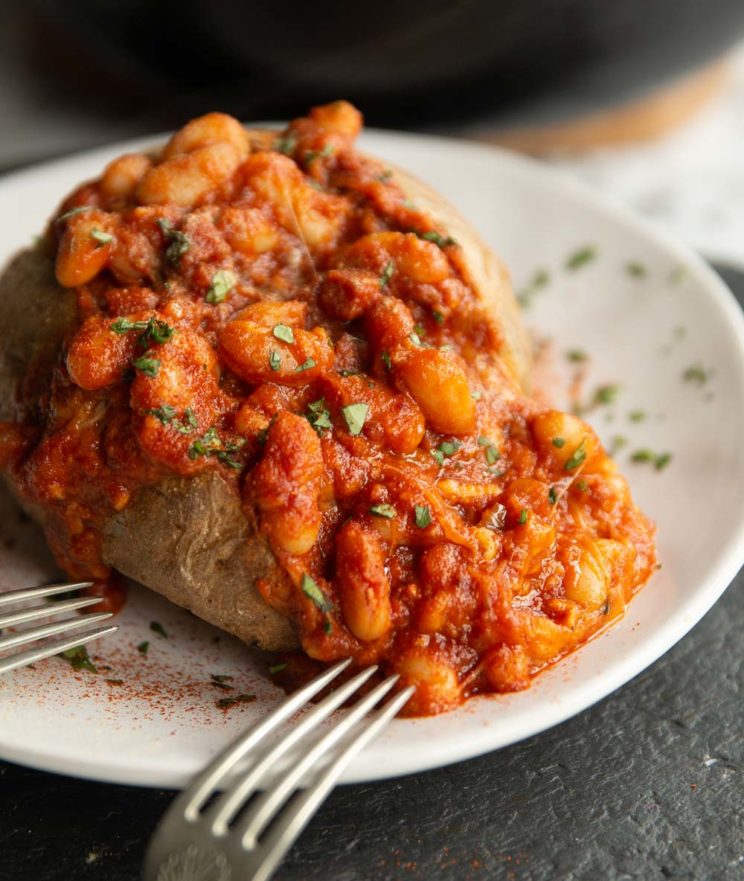 beans poured on baked potato on white plate with two silver forks resting