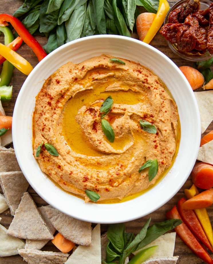 overhead shot of white bowl of hummus surrounded by veg and pita chips