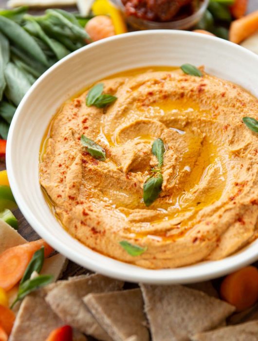 close up shot of hummus surrounded by vegetables and pita chips