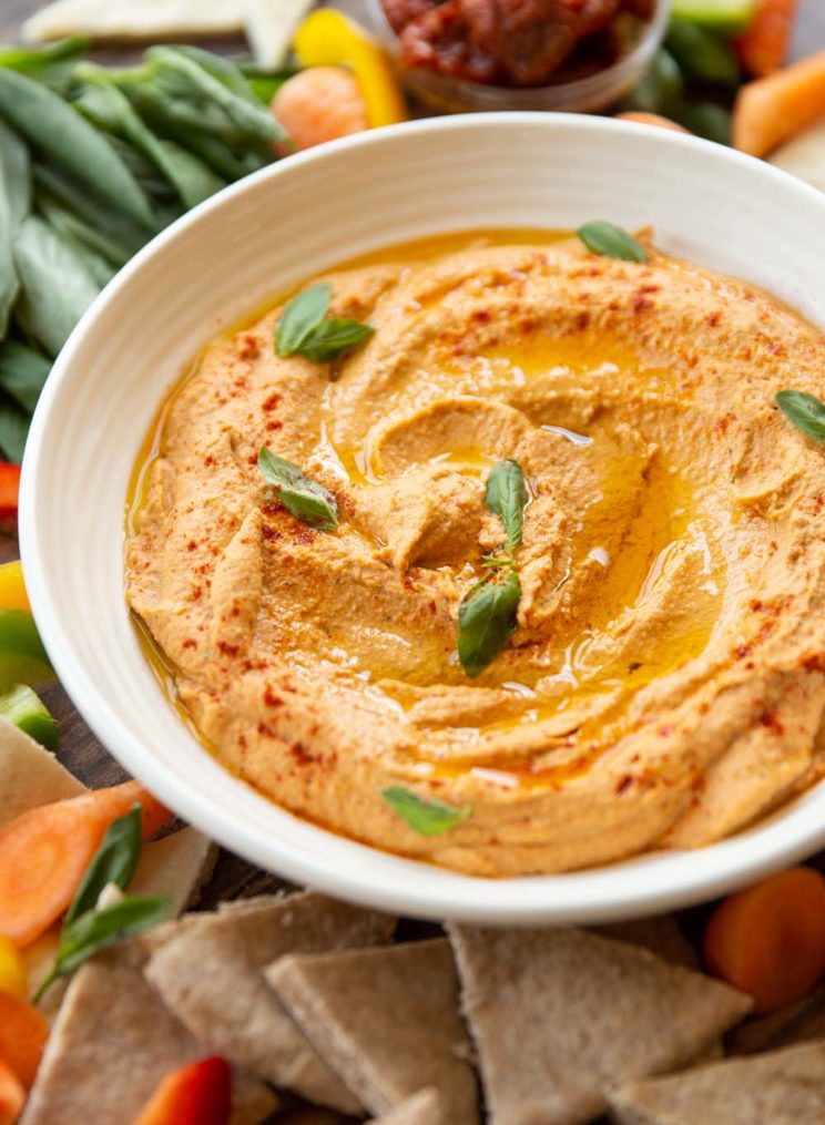 close up shot of hummus surrounded by vegetables and pita chips