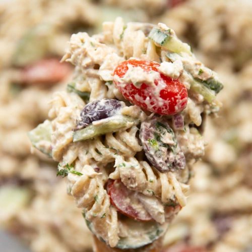 pasta salad resting on salad spoon held above bowl of salad