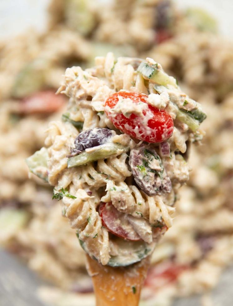 pasta salad resting on salad spoon held above bowl of salad