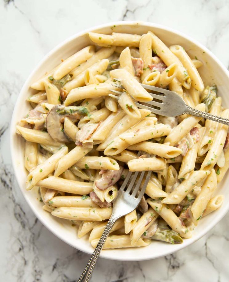 overhead shot of pasta served in white bowl with two silver forks digging in