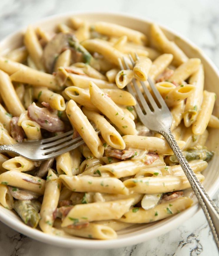 closeup shot of pasta served in bowl with two forks digging in