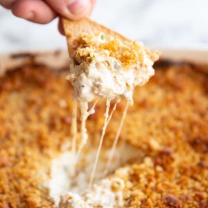 hand scooping out dip with tortilla chip with cheese pull