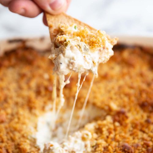 hand scooping out dip with tortilla chip with cheese pull