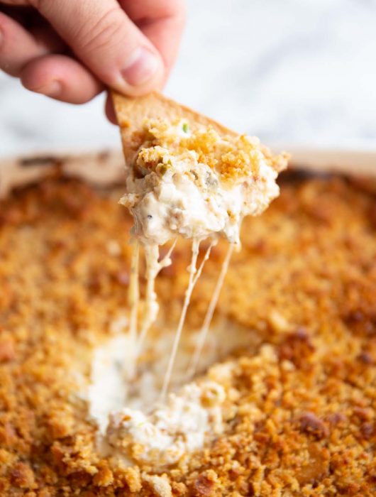 hand scooping out dip with tortilla chip with cheese pull