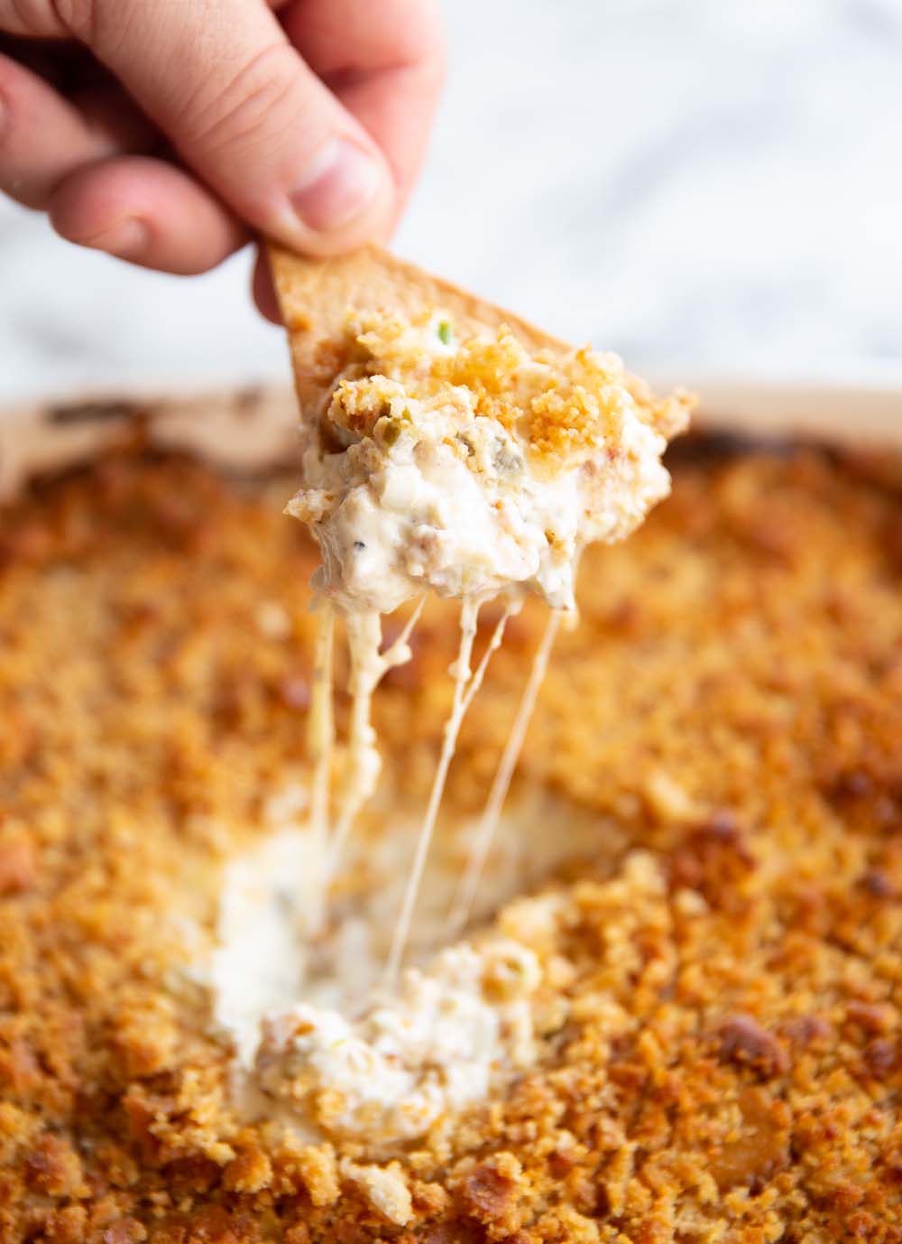 hand scooping out dip with tortilla chip with cheese pull