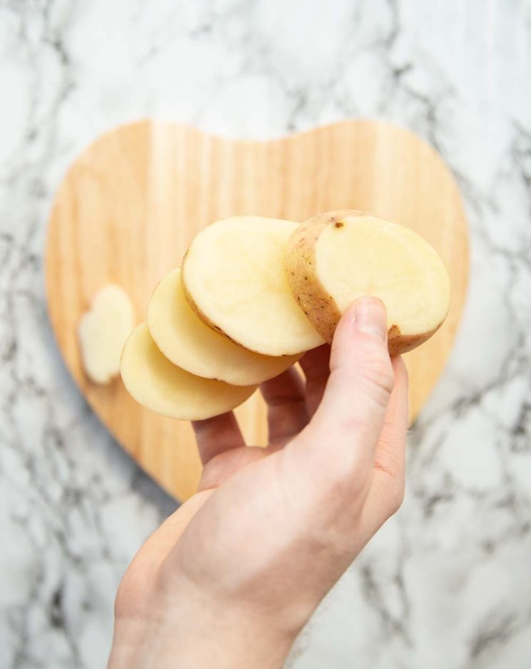 hand holding sliced potatoes above heart shaped chopping board