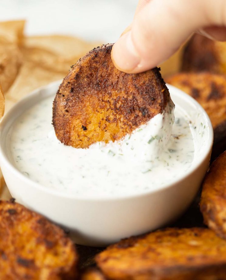 fingers dipping potato into white pot of dip