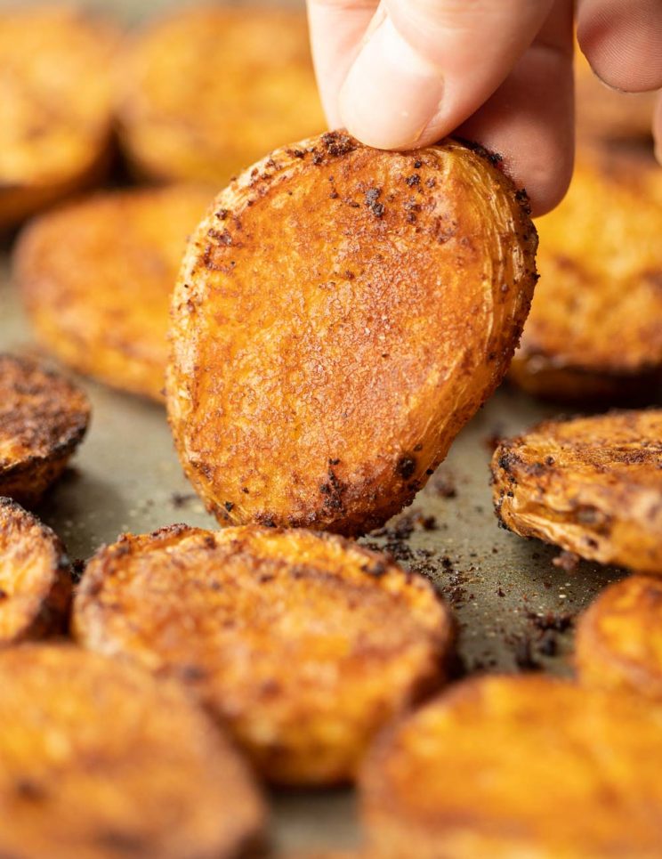 closeup shot of fingers holding up potato on baking tray