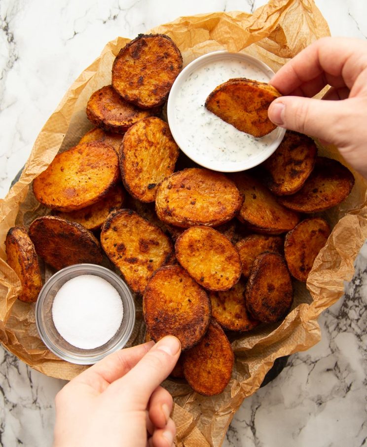 overhead shot of potatoes un scrunched paper with pot of dip and salt with hands reaching in