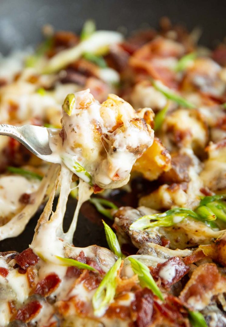 fork lifting potato out of pan with cheese dripping down