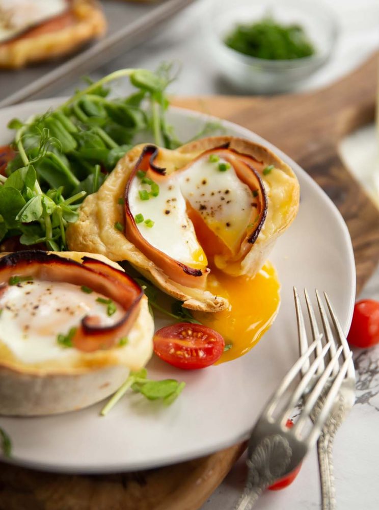 egg cup sliced open with yolk pouring out on plate served with salad and baby plum tomatoes